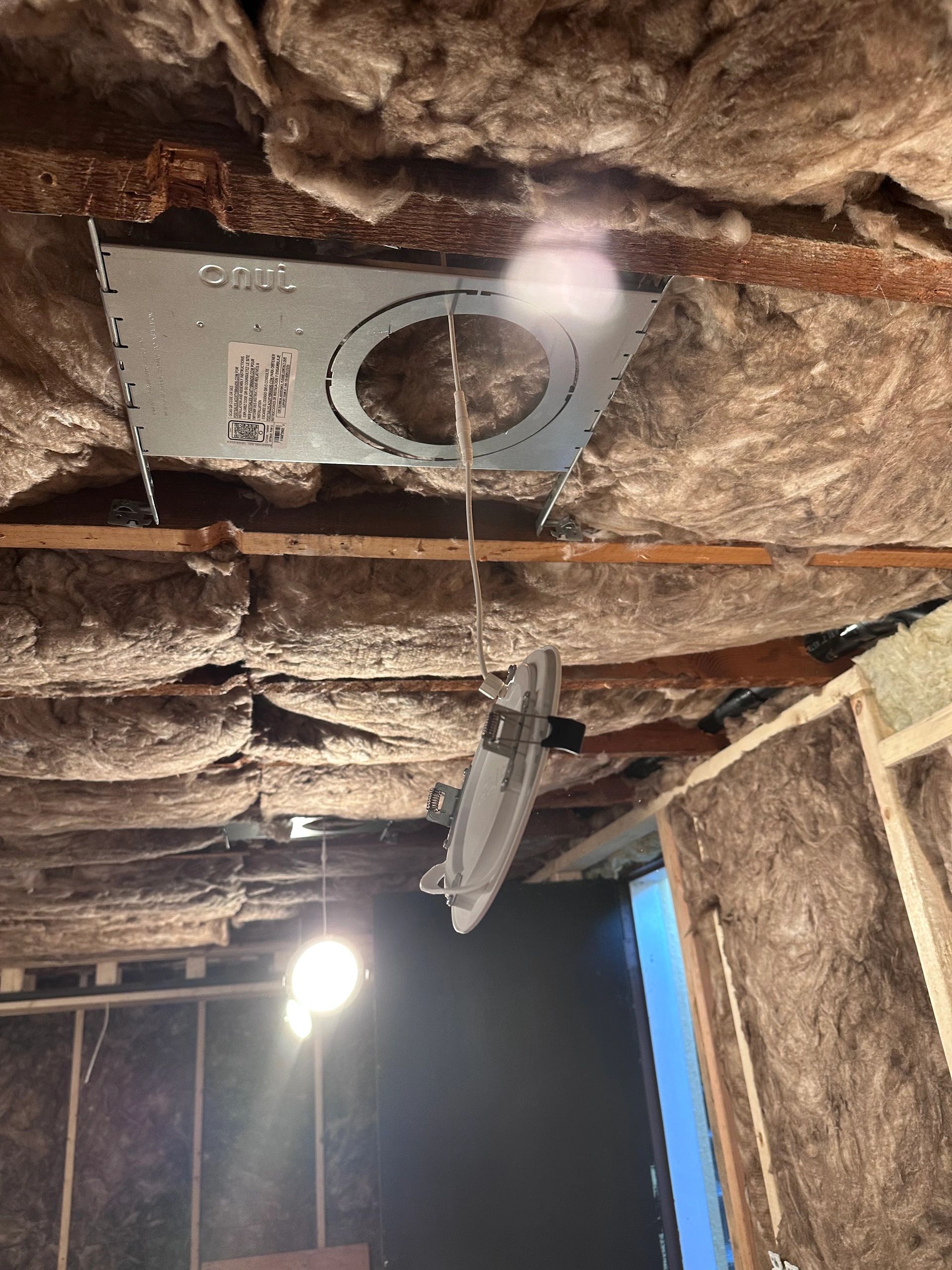 Recessed light housing installed between joists in an insulated ceiling during a remodel