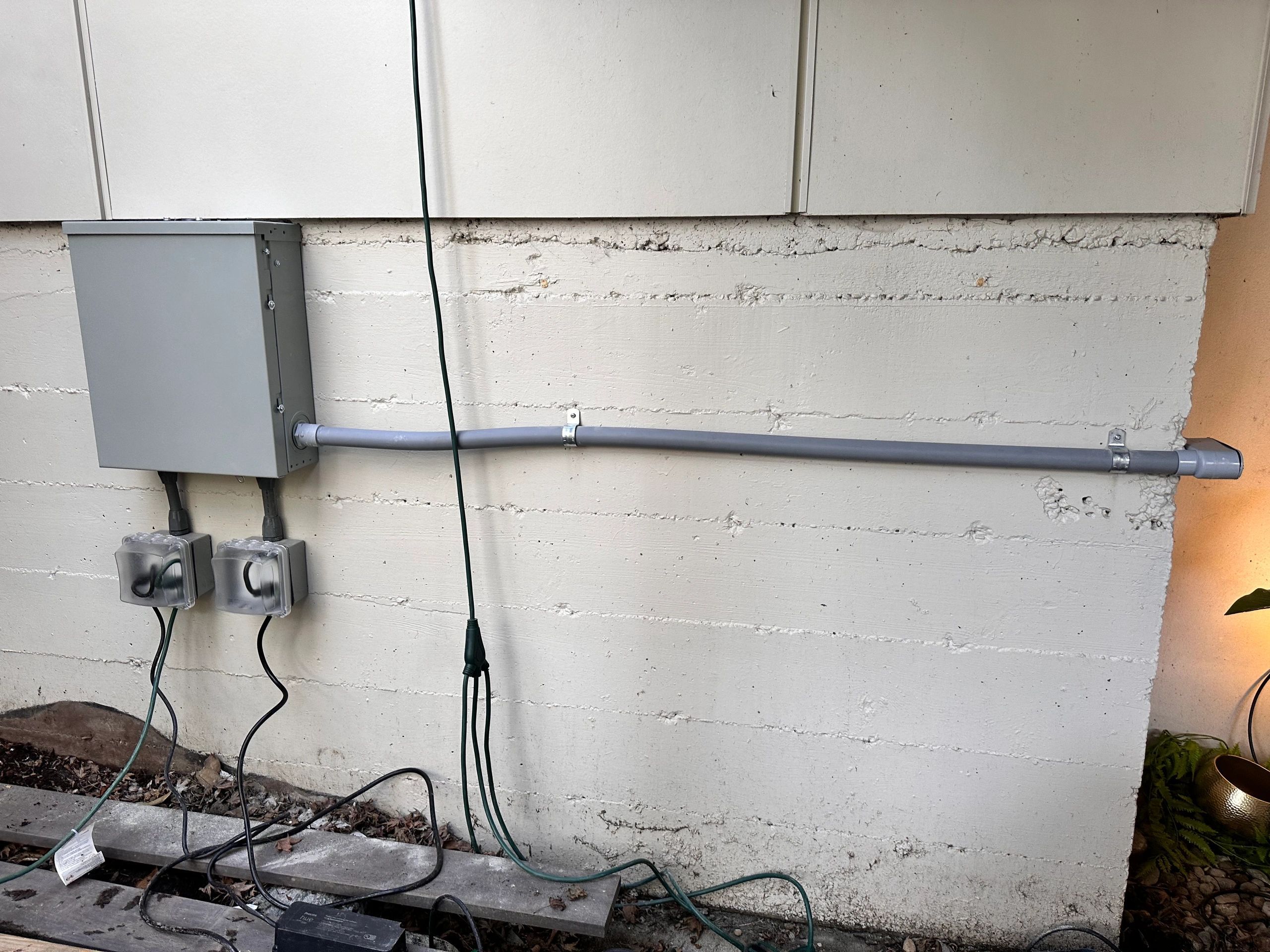 Exterior electrical enclosure with conduit run along a concrete foundation wall