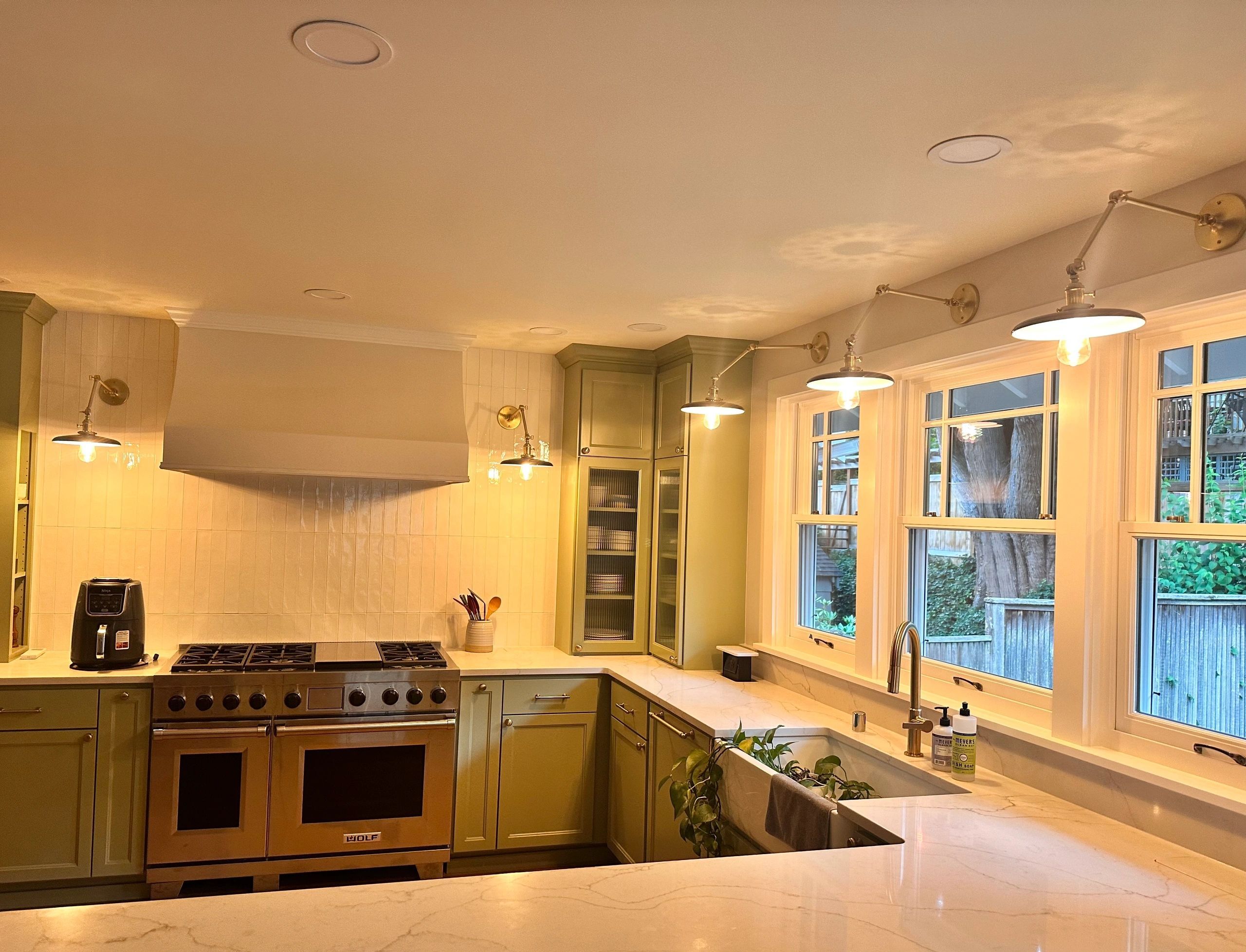 Kitchen with brass wall sconces over the windows and warm under-cabinet lighting