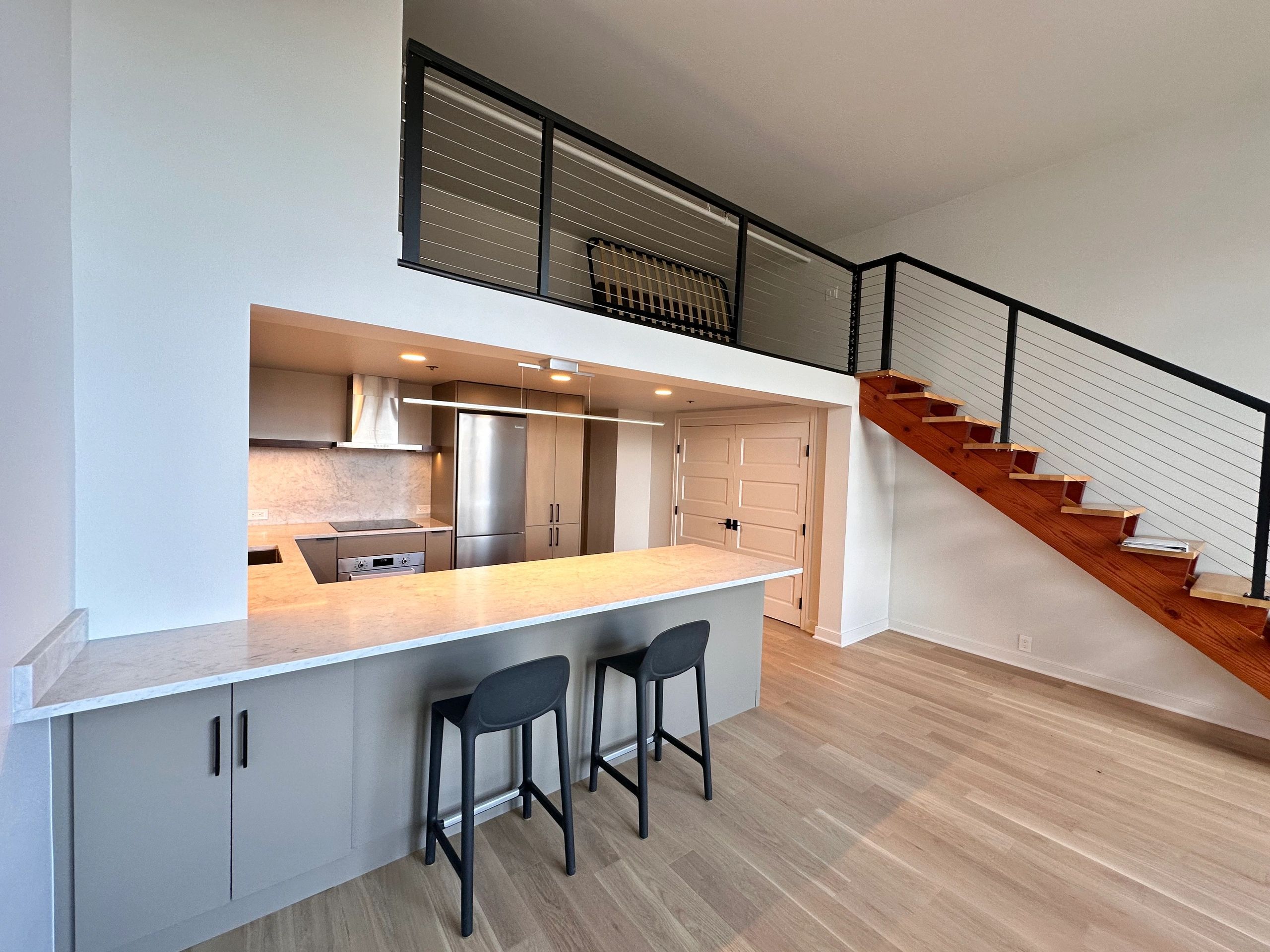 Modern kitchen with under-cabinet lighting below an open loft and staircase